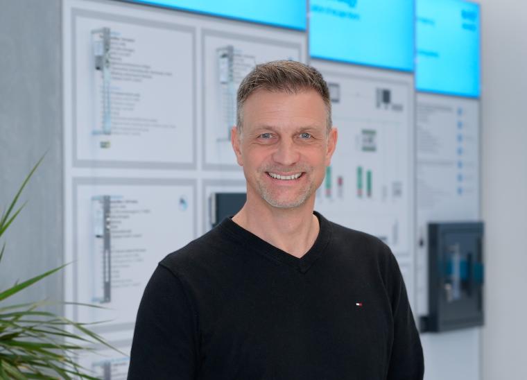 Person mit schwarzem Pullover steht vor einer Displaywand mit technischen...