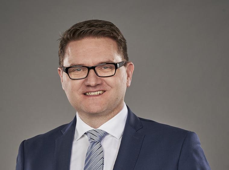 Porträt einer Person mit Brille im blauen Anzug und Krawatte vor neutralem...