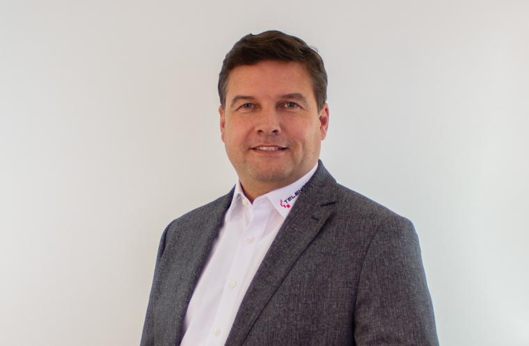 Porträt einer Person im grauen Sakko mit weißem Hemd vor hellem, neutralem...