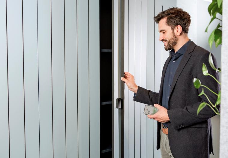 A man standing in front of a locker with a cell phone in his left hand
