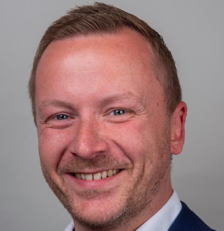 Portrait of a smiling man with three-day stubble, a blue blazer, and a white...