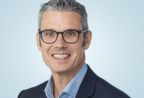 Portrait of a person wearing glasses and business attire, against a light...