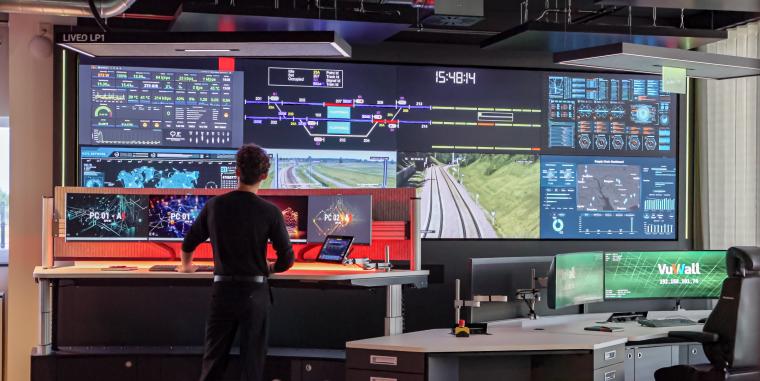 A man standing in front of a very wide wall of monitors displaying various views