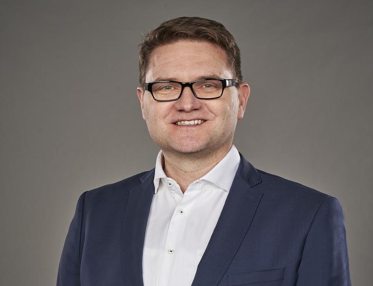 Jüngerer Mann mit Brille, blauem Anzug und weißem Hemd