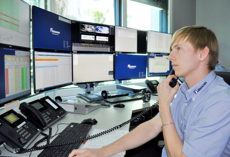 Junger Mann am Telefon vor Tisch mit Monitoren