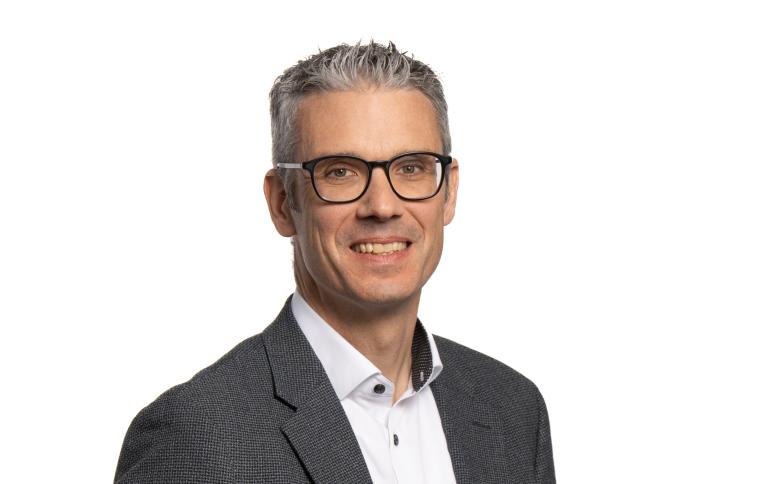Mann mit grauen Haaren, schwarzer Brille und grauem Anzug