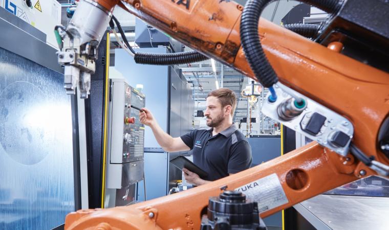 Person arbeitet an einer Schalttafel hinter einem Roboterarm