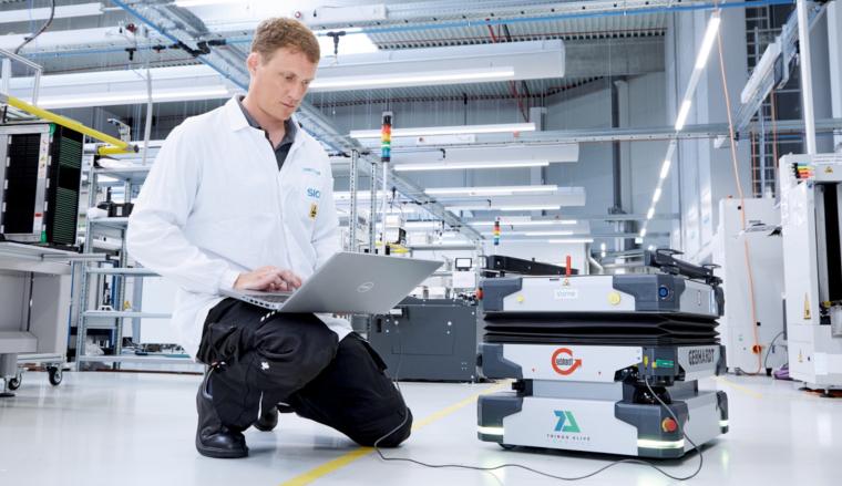 Person kniet mit Laptop in einer Fabrikhalle