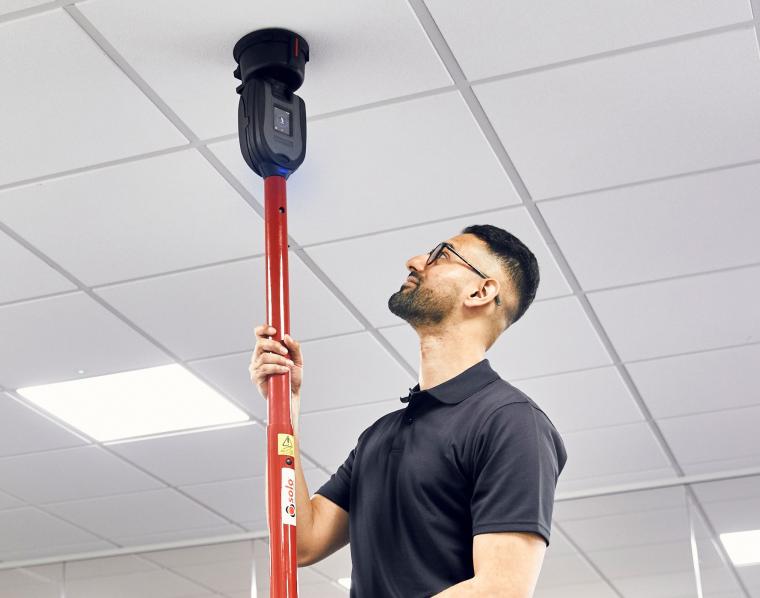 Person prüft mit einem Teleskopmast einen Sensor oder Melder an einer...