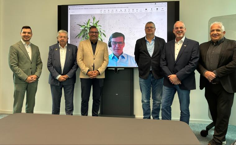 6 Männer plus noch einer auf einem Monitor, stehend