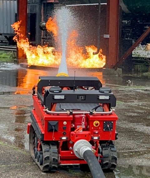 Ein roter Löschroboter auf Ketten schießt Löschwasser auf einen Testbrand