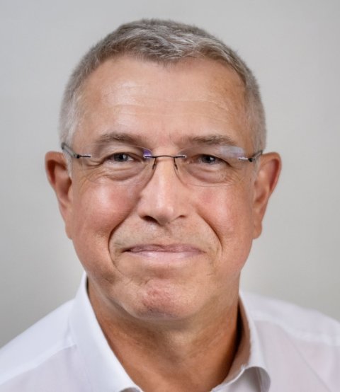 Person mit grauen Haaren und weißem Hemd vor hellem Hintergrund