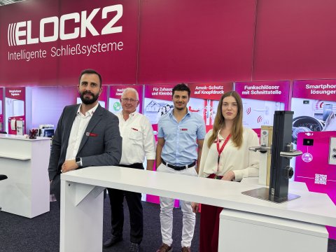 Drei Männer und eine Frau am Tresen eines Messestandes von Elock auf der Sicherheitsexpo