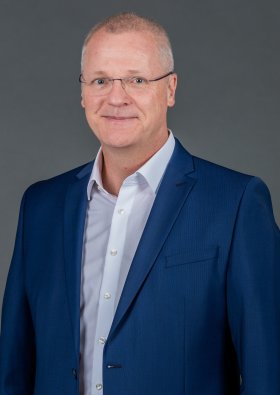 Mann mittleren Alters stehend mit kurzen Haaren, blauem Sakko und Jeans