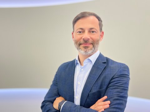 Middle-aged man with a short beard wearing a blue shirt and dark blue jacket looks into the camera