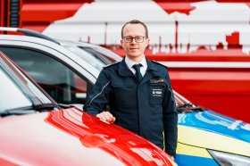 Mittelalter Mann mit blauer Uniform der zwischen Einsatzautos steht