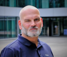 Eine Person in einem dunkelblauen Firmenpoloshirt steht vor einem modernen Bürogebäude