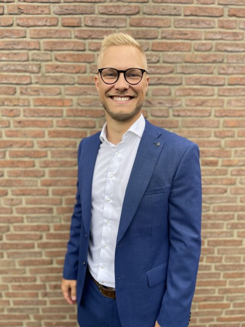 Portrait Jan Gundermann, lächelnd mit kurzem, blondem Haar, dunkler Brille und blauem Anzug