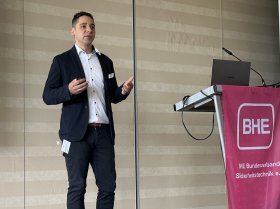 Junger Mann mit dunklem Anzug und weißem Hemd bei einem Vortrag