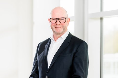 Mittelalter Mann mit Glatze, Brille, dunklem Sakko und weißem Hemd