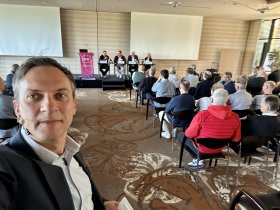 Mittelalter Mann mit Headset in einem Saal mit Menschen und Podium im Hintergrund