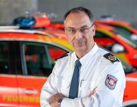 Mann mit Feuerwehruniform mit Feuerwehrautos im Hintergrund
