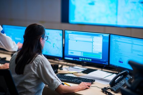 Frau von hinten in einem Kontrollraum mit Monitoren
