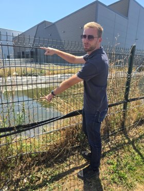 Schlanker Mann mit kurzem blauen Hemd und Sonnenbrille hantiert an Zaun