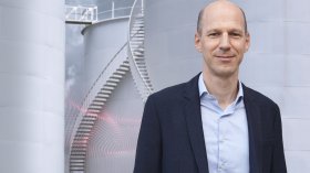 Person standing in front of industrial tanks with external staircase and sensor data visualization
