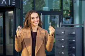 Resident holding a traditional keyring and a digital access key beside apartment mailboxes.