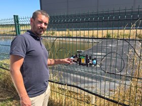 A man wearing a blue polo shirt points to a splice sleeve built into a fence
