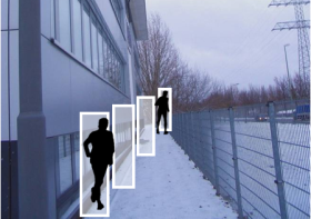 Figuren in weißen Kästen hervorgehoben vor Fassade mit Videokamera