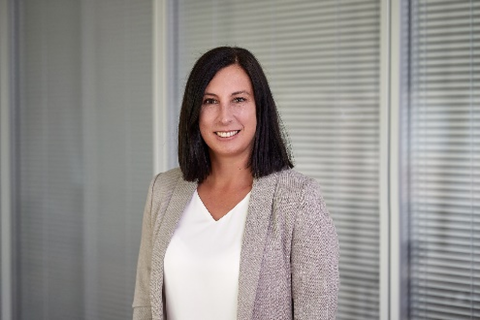 A woman with shoulder-length dark hair, a beige blazer, and a white shirt